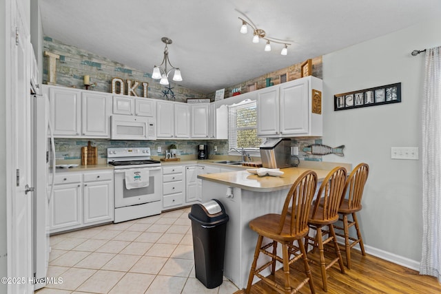 169 NW 7th St, Oak Island, NC 28465 - kitchen featuring white appliances, a peninsula, light countertops, backsplash, and white cabinets
