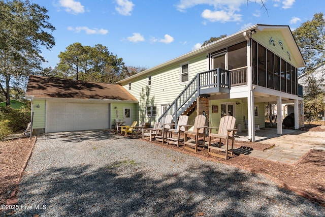 view of front of home with a patio, a garage, a sunroom, stairs, and gravel driveway