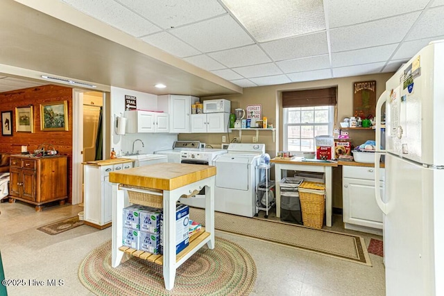 kitchen with a sink, white cabinets, freestanding refrigerator, light floors, and washer and clothes dryer