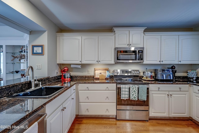 kitchen with dark stone countertops, a sink, appliances with stainless steel finishes, and white cabinetry