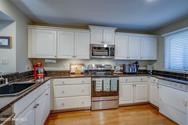 kitchen with light wood-style flooring, a sink, white cabinetry, dark stone counters, and appliances with stainless steel finishes