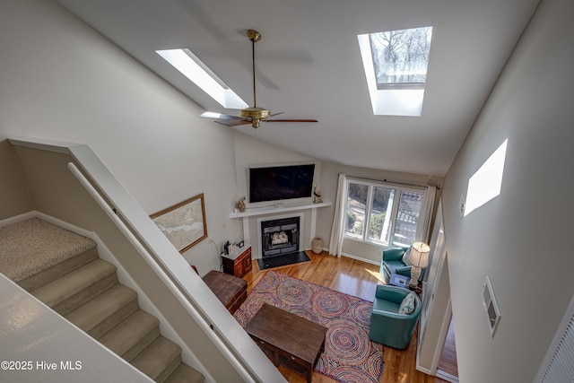 living room with stairway, a skylight, a fireplace with flush hearth, and wood finished floors