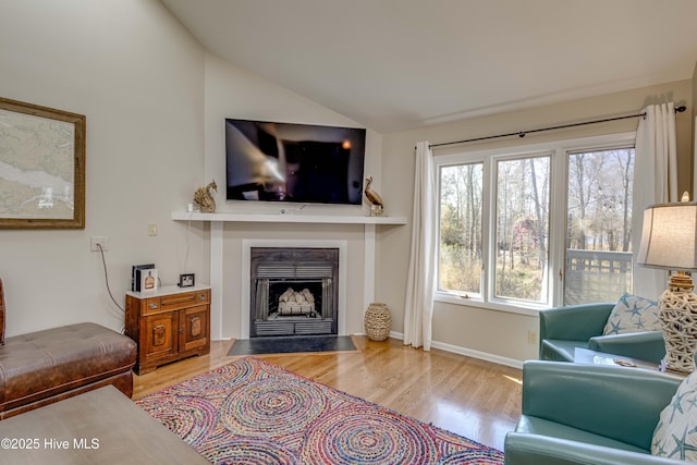 living area with vaulted ceiling, baseboards, a fireplace with flush hearth, and wood finished floors