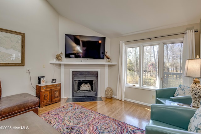 living area with lofted ceiling, wood finished floors, baseboards, and a fireplace with flush hearth