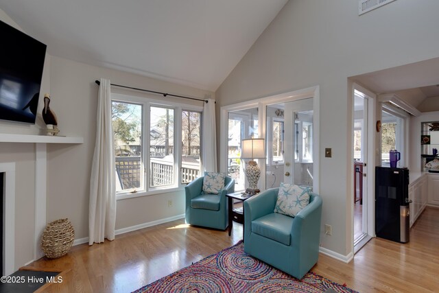 living area featuring visible vents, light wood-style floors, baseboards, and high vaulted ceiling