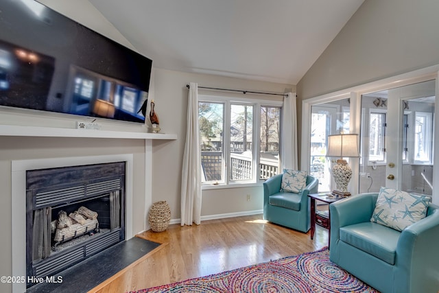 living area featuring baseboards, wood finished floors, a fireplace with flush hearth, and lofted ceiling
