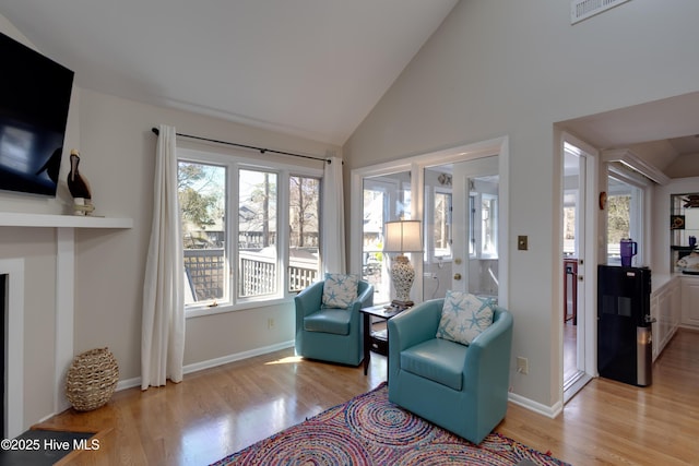 living area with visible vents, light wood-type flooring, high vaulted ceiling, and baseboards