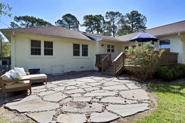 back of property with brick siding, roof with shingles, a deck, crawl space, and a patio