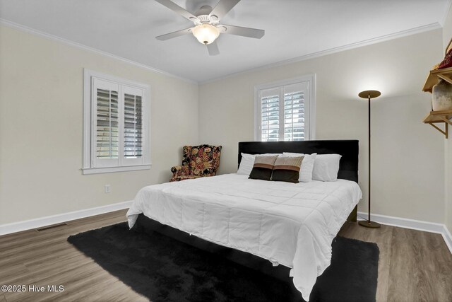 bedroom with wood finished floors, visible vents, baseboards, ceiling fan, and crown molding