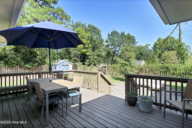 wooden deck featuring an outbuilding, outdoor dining space, a shed, and a fenced backyard
