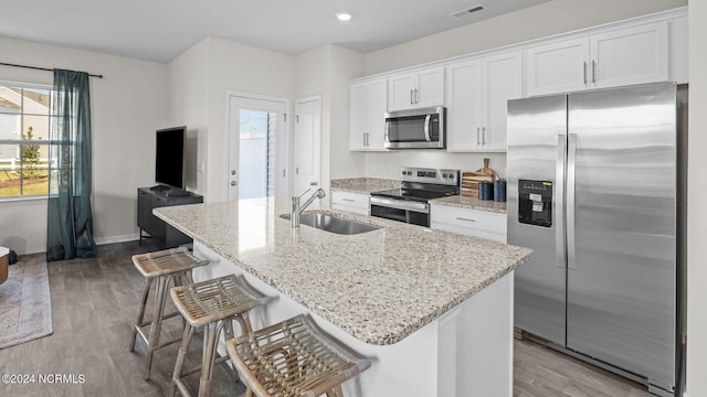 kitchen with stainless steel appliances, white cabinetry, a center island with sink, and a breakfast bar area