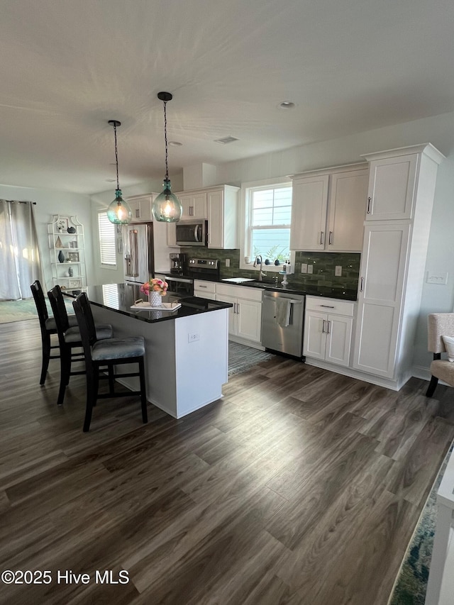 kitchen with stainless steel appliances, a kitchen island, decorative backsplash, dark wood-style floors, and dark countertops