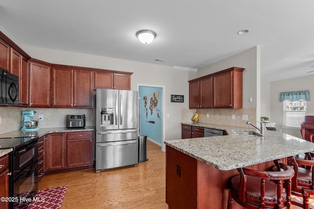 kitchen featuring light stone counters, a peninsula, light wood-style floors, a kitchen breakfast bar, and black appliances