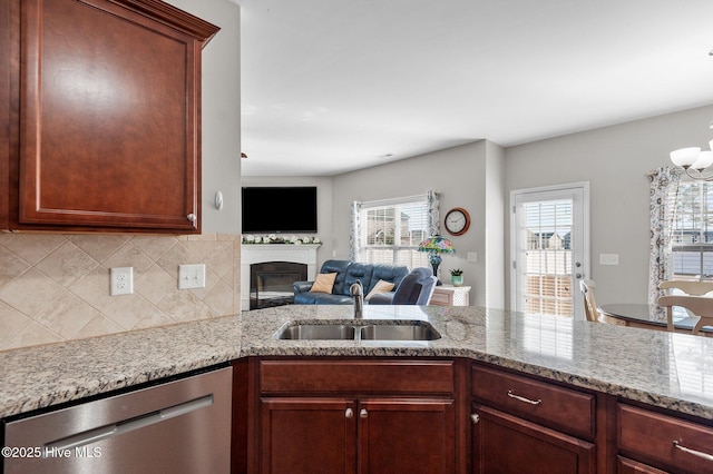 kitchen with decorative backsplash, dishwasher, a glass covered fireplace, open floor plan, and a sink