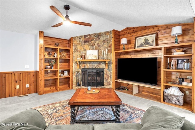 carpeted living room featuring a fireplace, wooden walls, vaulted ceiling, and a textured ceiling