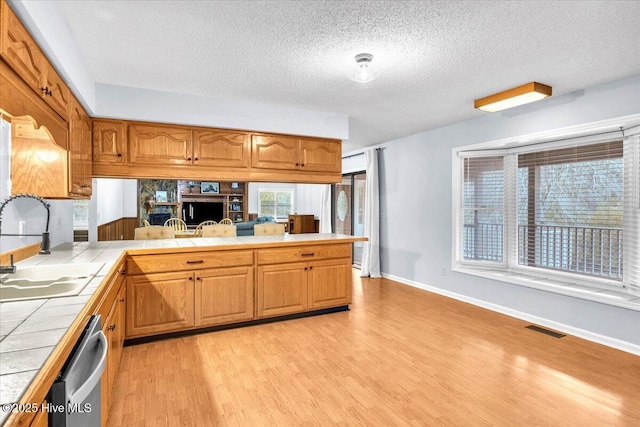 kitchen featuring sink, dishwasher, tile counters, a textured ceiling, and light wood-type flooring