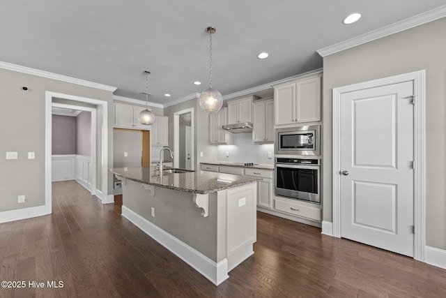 kitchen with a center island with sink, stainless steel appliances, sink, stone countertops, and pendant lighting