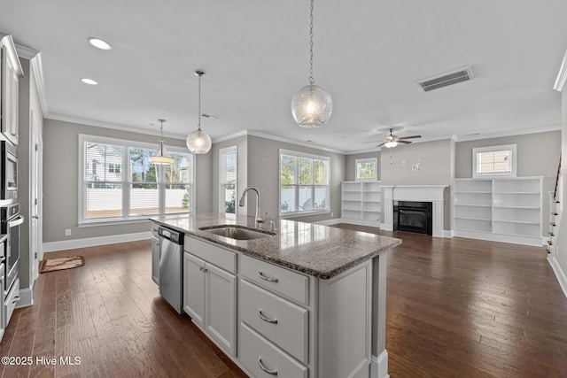 kitchen featuring a center island with sink, appliances with stainless steel finishes, light stone countertops, decorative light fixtures, and sink