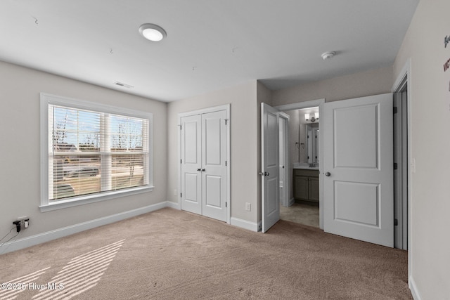 unfurnished bedroom with a closet, light colored carpet, and ensuite bath