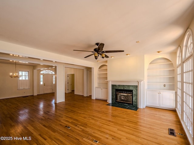 unfurnished living room with visible vents, light wood-type flooring, built in shelves, a fireplace, and ceiling fan with notable chandelier