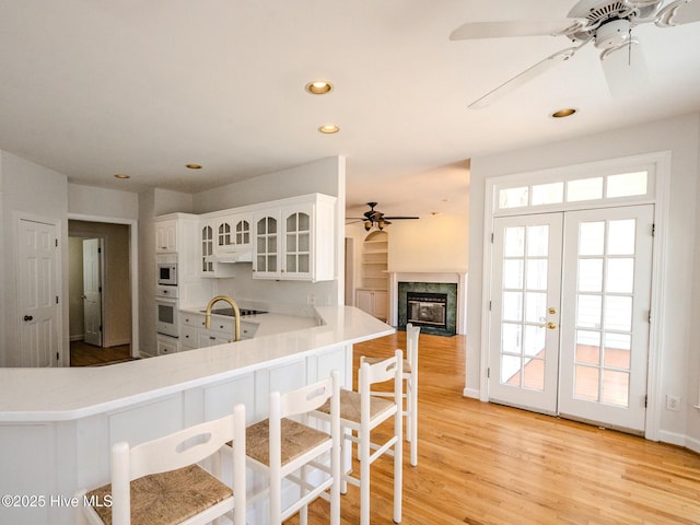 kitchen featuring french doors, light wood finished floors, white cabinetry, white appliances, and under cabinet range hood