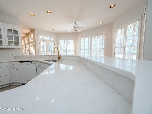 kitchen featuring recessed lighting, glass insert cabinets, white dishwasher, a sink, and light stone countertops