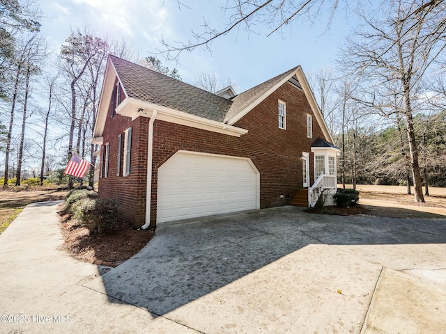 view of side of property with driveway, roof with shingles, a garage, and brick siding