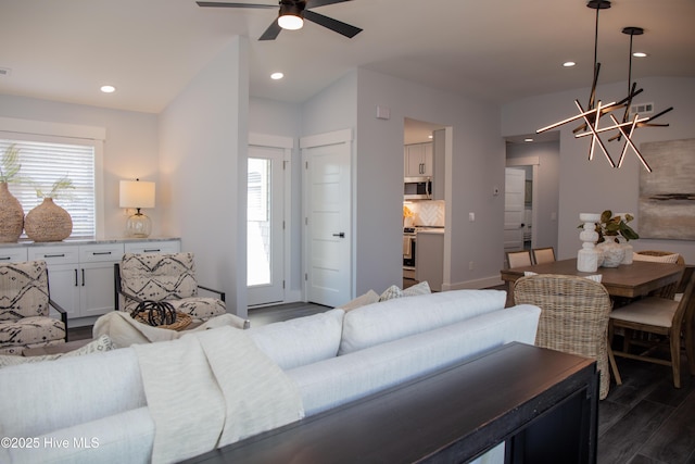 living room featuring dark wood-type flooring, a wealth of natural light, and ceiling fan with notable chandelier