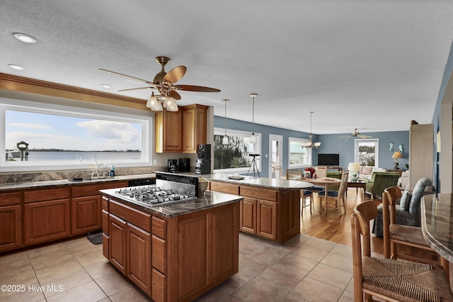 kitchen with stainless steel gas cooktop, a water view, a center island, brown cabinets, and decorative light fixtures