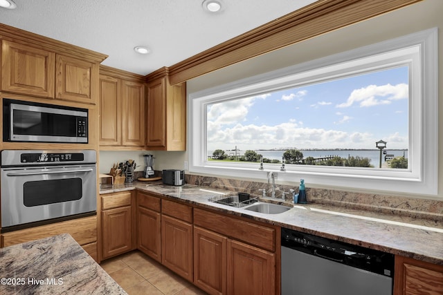 kitchen featuring light tile patterned floors, stainless steel appliances, a water view, brown cabinetry, and a sink