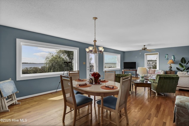 dining space with light wood-type flooring, a textured ceiling, baseboards, and ceiling fan with notable chandelier