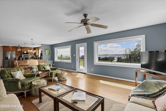 living area with a textured ceiling, light wood finished floors, ceiling fan with notable chandelier, and baseboards