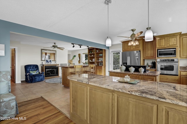 kitchen featuring light stone counters, decorative light fixtures, stainless steel appliances, open floor plan, and a textured ceiling