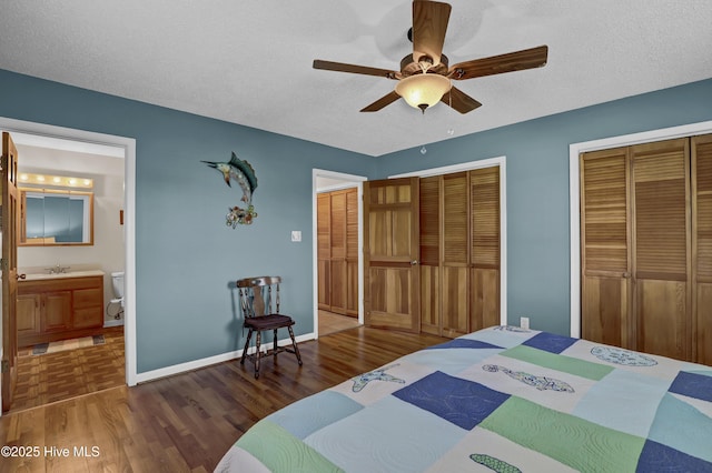 bedroom featuring dark wood-style floors, a textured ceiling, baseboards, and multiple closets