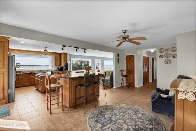 kitchen featuring a breakfast bar, freestanding refrigerator, brown cabinets, and light tile patterned floors