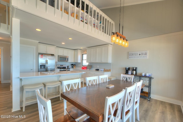 dining area featuring ornamental molding, a towering ceiling, sink, and light wood-type flooring