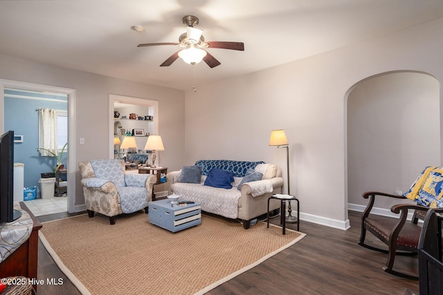 living room featuring dark wood-type flooring, ceiling fan, and built in shelves