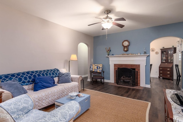 living room with dark wood-type flooring, ceiling fan, and a fireplace