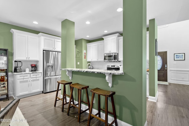 kitchen with light stone counters, light wood-type flooring, a kitchen breakfast bar, stainless steel appliances, and white cabinets