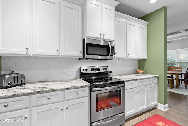 kitchen with white cabinetry, appliances with stainless steel finishes, light stone countertops, light hardwood / wood-style floors, and backsplash