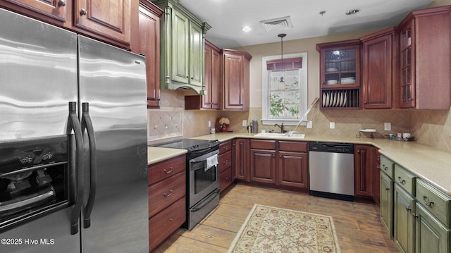 kitchen featuring appliances with stainless steel finishes, tasteful backsplash, sink, hanging light fixtures, and light hardwood / wood-style floors