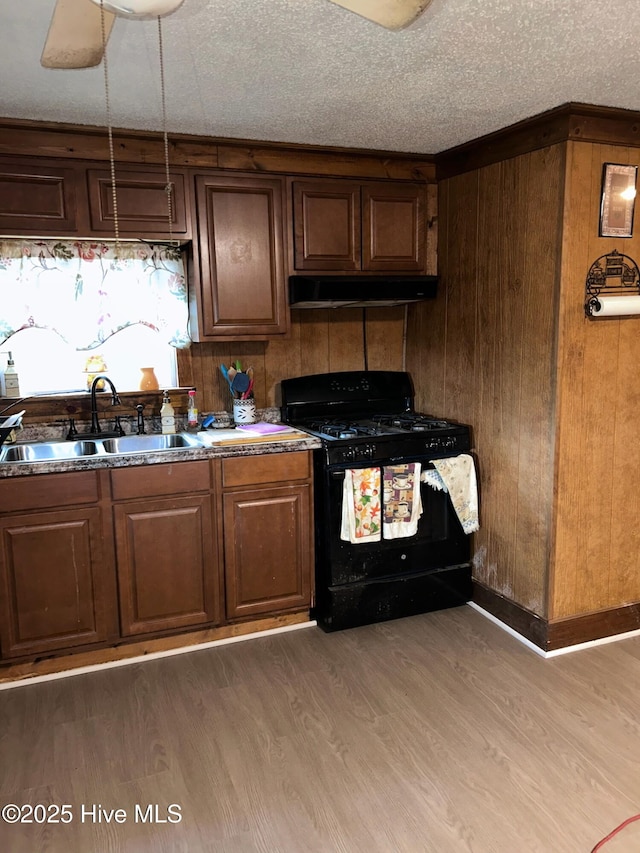 kitchen featuring light wood-style flooring, a sink, black range with gas cooktop, under cabinet range hood, and a textured ceiling