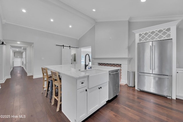 kitchen featuring stainless steel appliances, a barn door, white cabinetry, a sink, and an island with sink