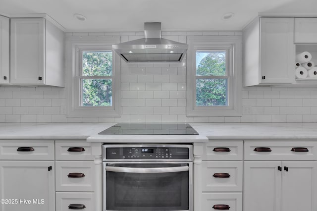 kitchen featuring decorative backsplash, light stone counters, oven, ventilation hood, and white cabinetry