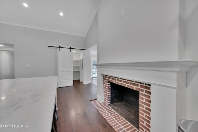 unfurnished living room featuring a barn door, dark wood-style flooring, baseboards, a brick fireplace, and crown molding