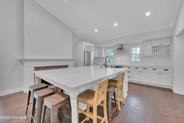 kitchen with a breakfast bar, white cabinets, a kitchen island with sink, and wall chimney exhaust hood