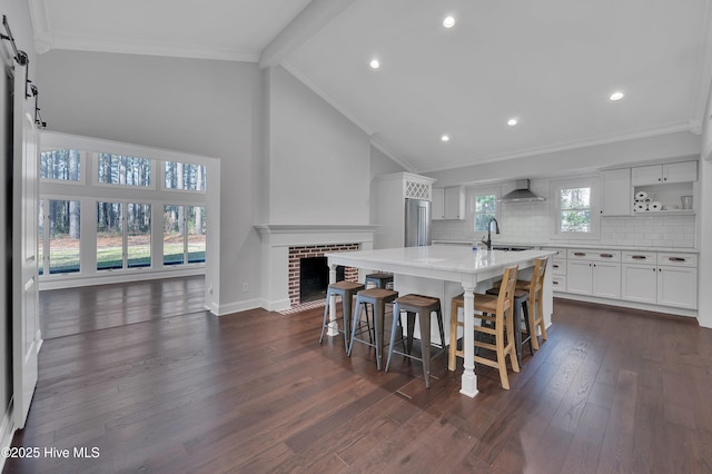 kitchen with light countertops, decorative backsplash, white cabinets, wall chimney range hood, and an island with sink