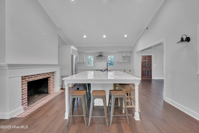 kitchen featuring dark wood-style flooring, high end refrigerator, white cabinetry, light countertops, and wall chimney range hood