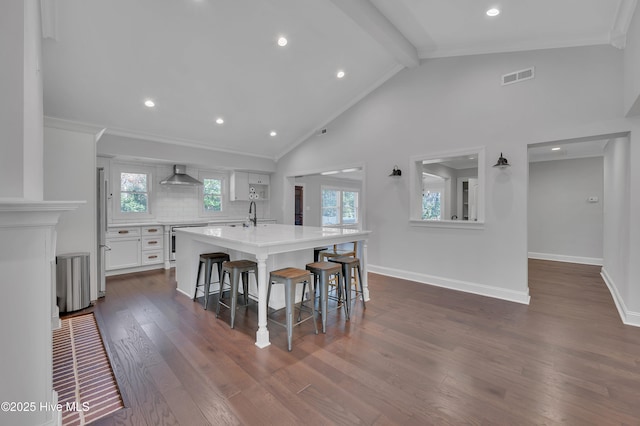 kitchen with a breakfast bar area, visible vents, white cabinets, light countertops, and wall chimney exhaust hood