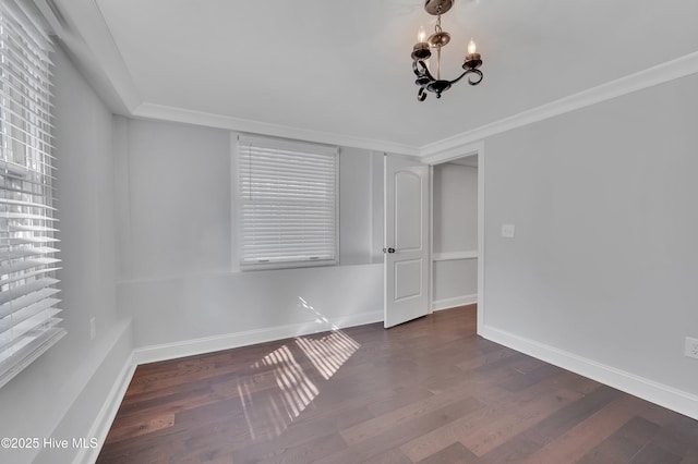 empty room featuring dark wood-style floors, a chandelier, crown molding, and baseboards